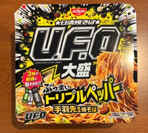 日清焼そばUFO大盛ぶっ濃いトリプルペッパー手羽先風味焼そばの写真。容器が四角いタイプのカップ焼きそばが、木目調のテーブルの上に置かれています。