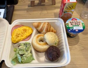ベーグル、枝豆のパン、クロワッサン、チョコマフィン、オムレツ、ハム、サラダのお弁当。ヨーグルトとオレンジジュースも。
